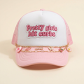 Front view of pink Curbs N Kisses trucker hat with embroidered patch and gold charm chains on a cream background