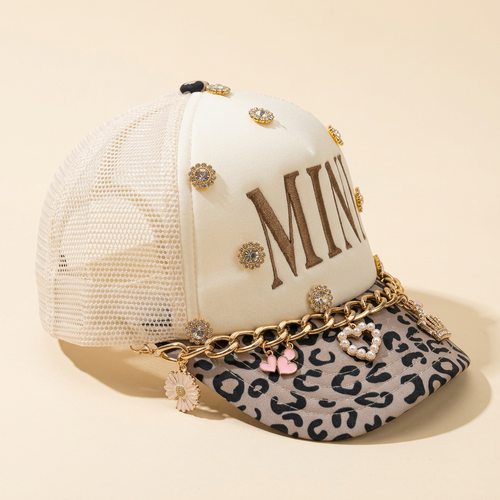 Side detail of Crowned Together Mini hat with leopard-print brim, gold chain and charms on a cream background