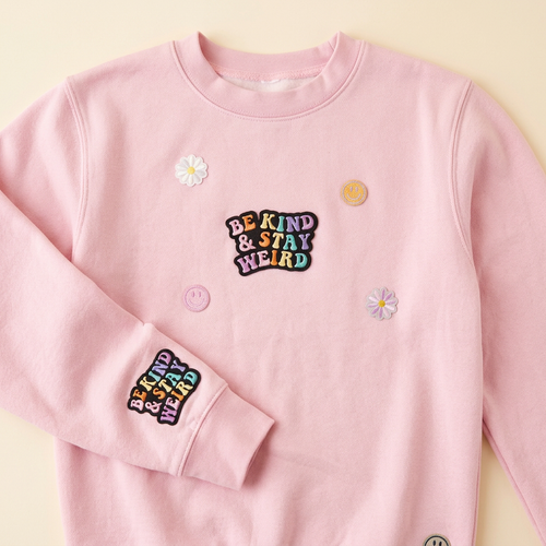Pink Kind N Quirky sweatshirt with embroidered patches against a warm cream background